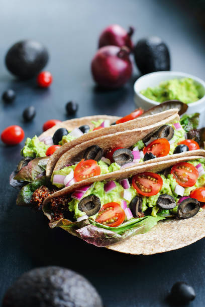 A healthy lunch or dinner of a vegan / vegetarian soft shell taco wrap made with red quinoa with taco season, romaine lettuce, sliced tomatoes, guacamole, black olives and red onions. Selective focus. High Protein Vegan Dinner Ideas-Top 10 Easy Recipes