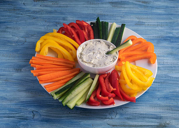 Colorful vegetable sticks in a plate with dip sauce on blue table